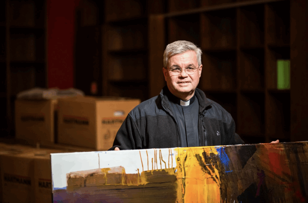 Erzbischof Dr. Udo Bentz steht vor Umzugskisten und hält ein großes Bild in den Händen